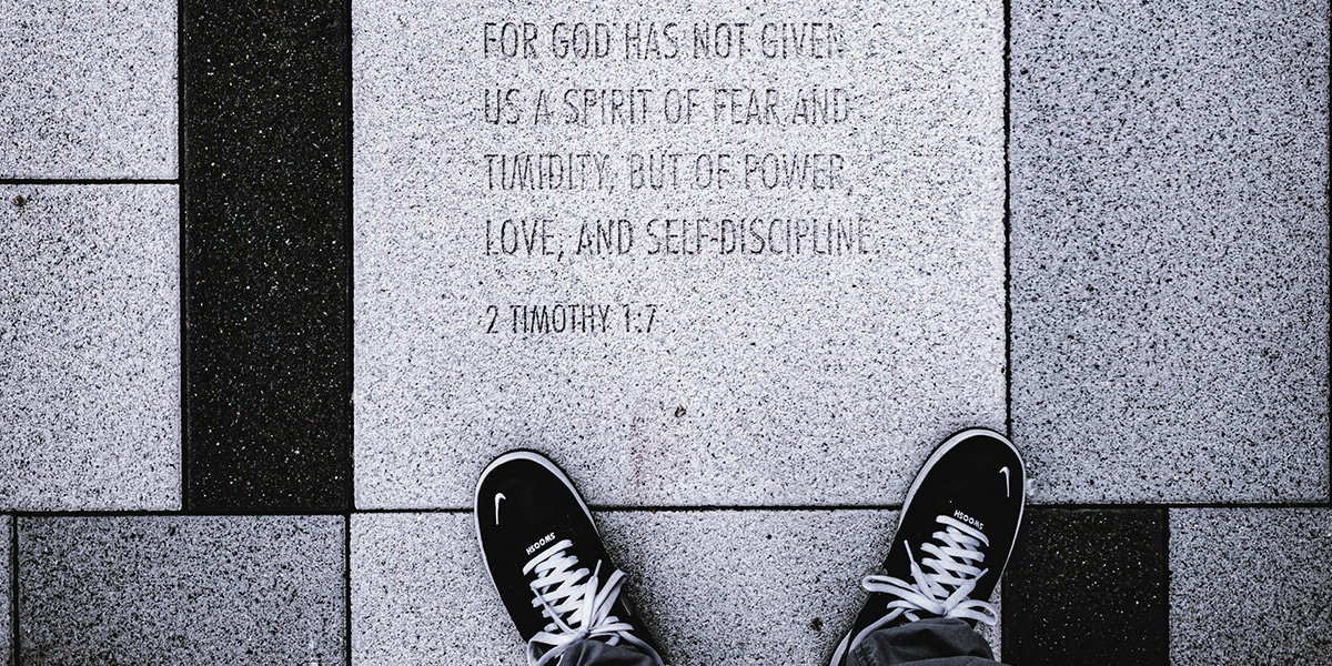 black sneakers standing next to a bible verse engraved in stone tile.