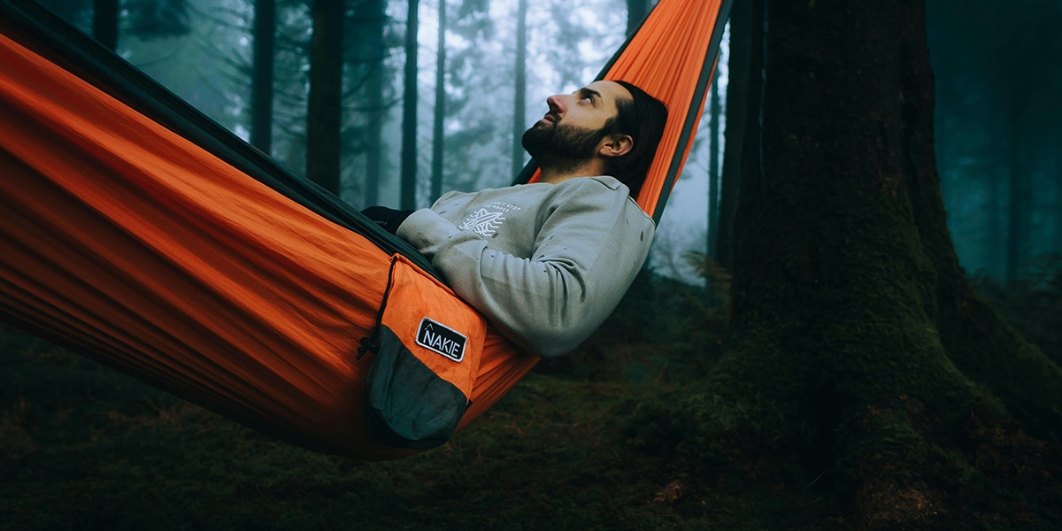 man resting in a hammock in the middle of a forest.
