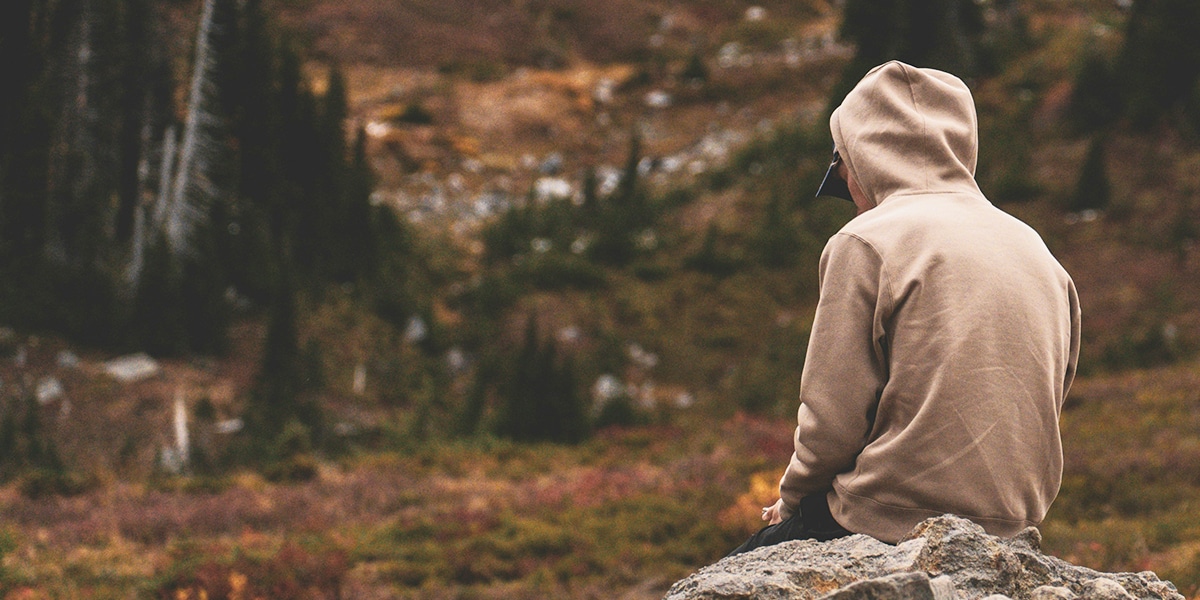 A man sitting on a rock, hiding his face in sadness and guilt.