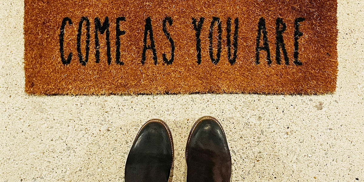 shoes in front of a welcome rug with the words "Come as you are" printed on it.