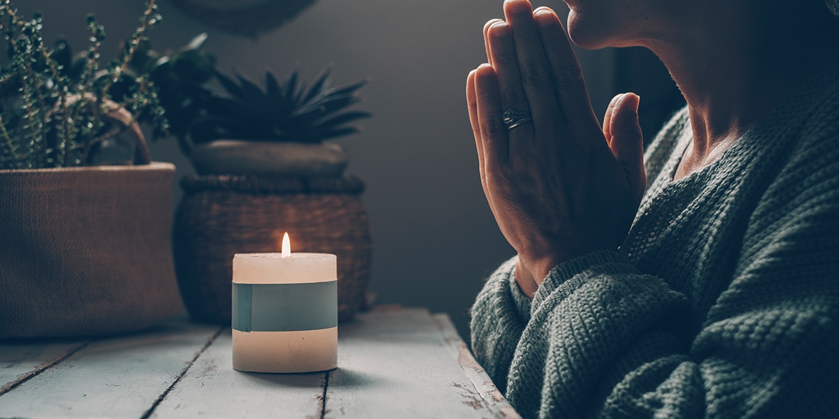 woman praying with folded hands in front of a candle